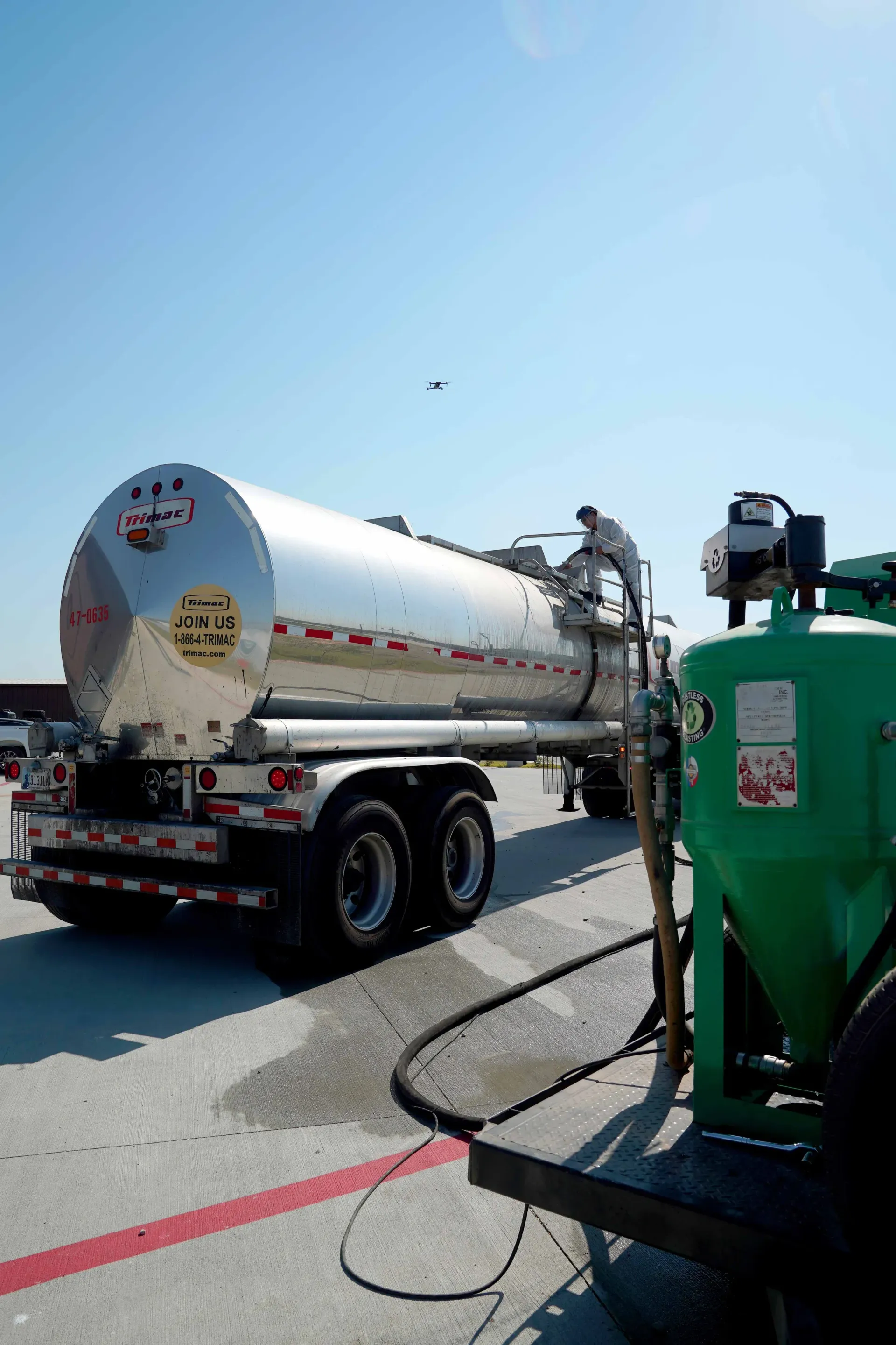 A tanker truck is parked on the side of the road next to a green machine.
