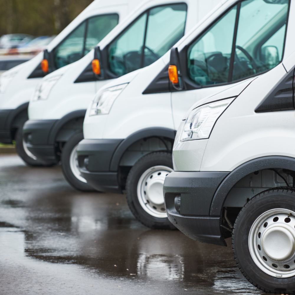 A row of white vans are parked in a parking lot