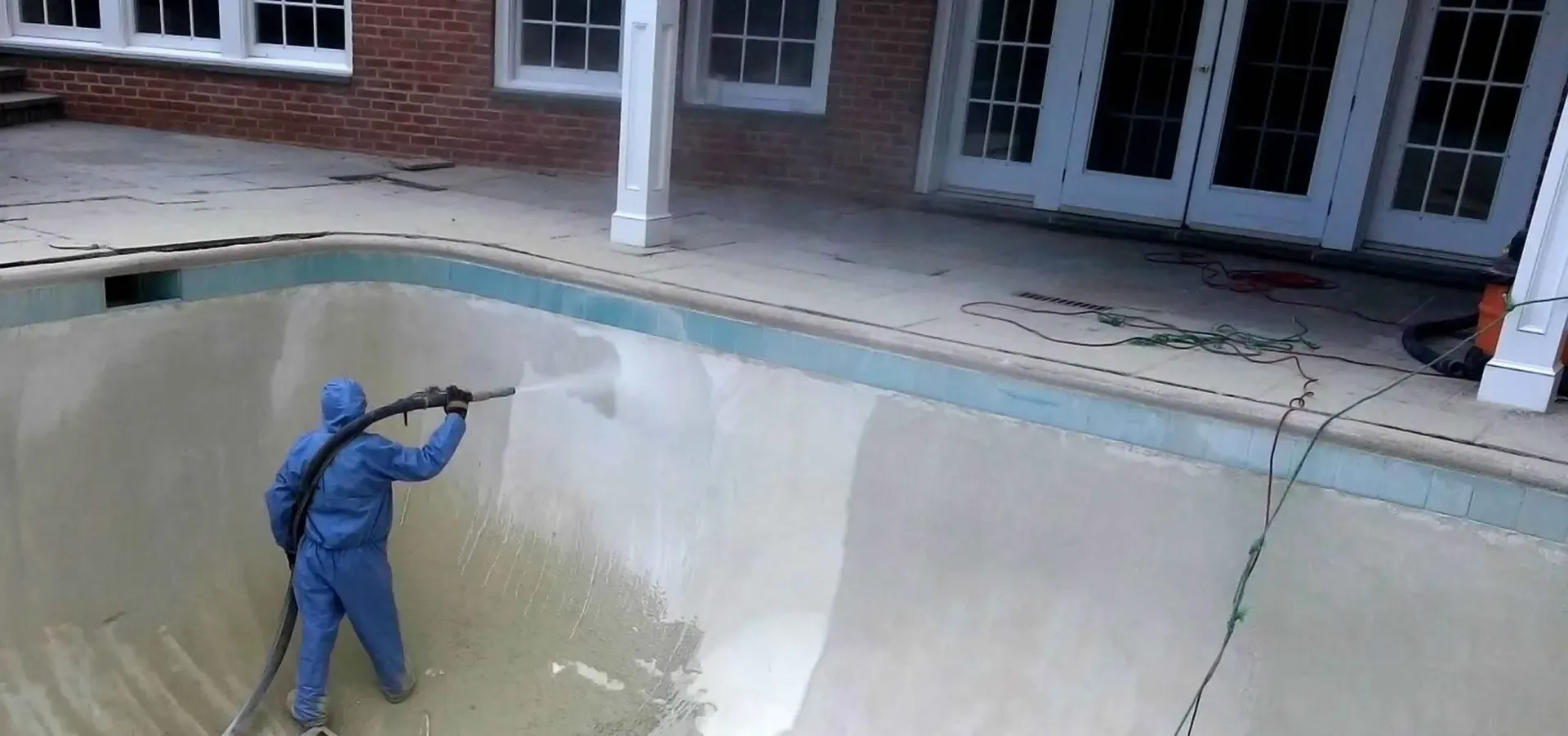 A man in a blue suit is cleaning a swimming pool.