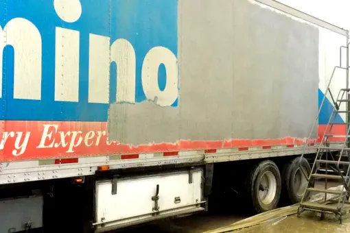 A truck with a commercial graphic on the side, halfway stripped off by a sandblaster.