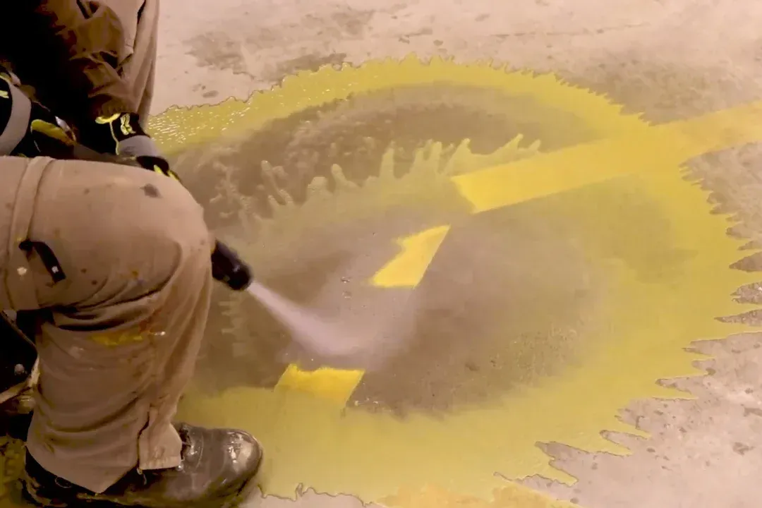 A person is spraying yellow paint on a concrete surface.