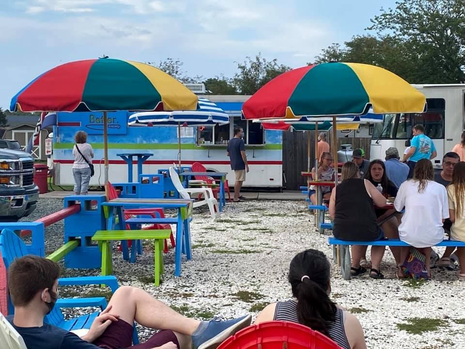 A group of people are sitting at picnic tables under colorful umbrellas