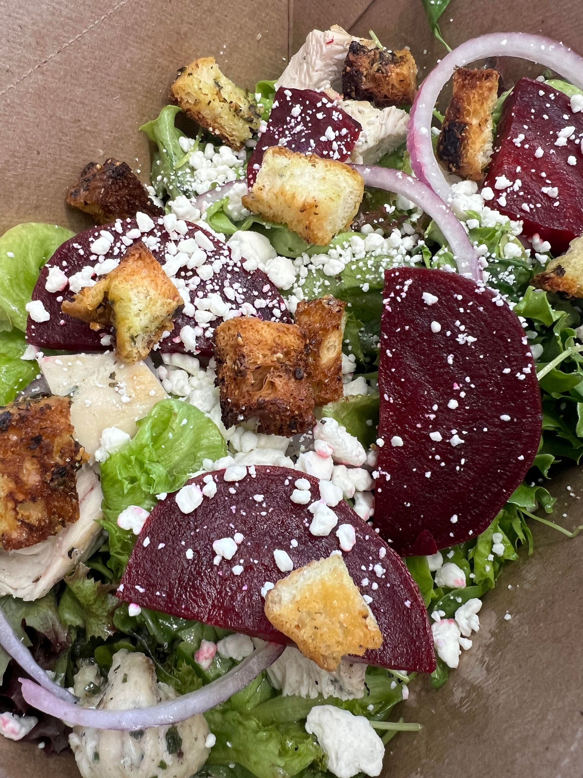 A close up of a salad with beets , croutons , onions and cheese