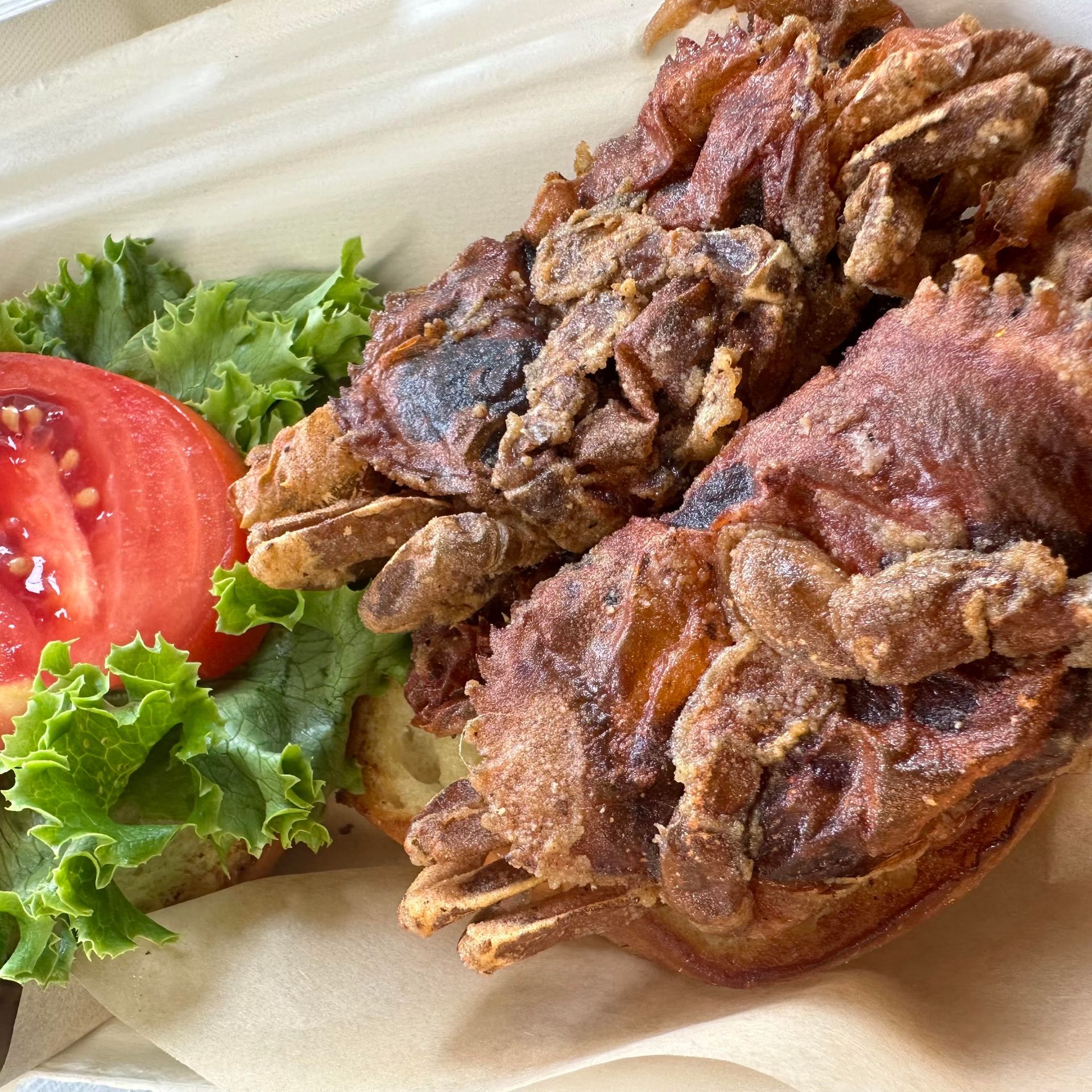 A fried chicken sandwich with lettuce and tomato on a styrofoam container