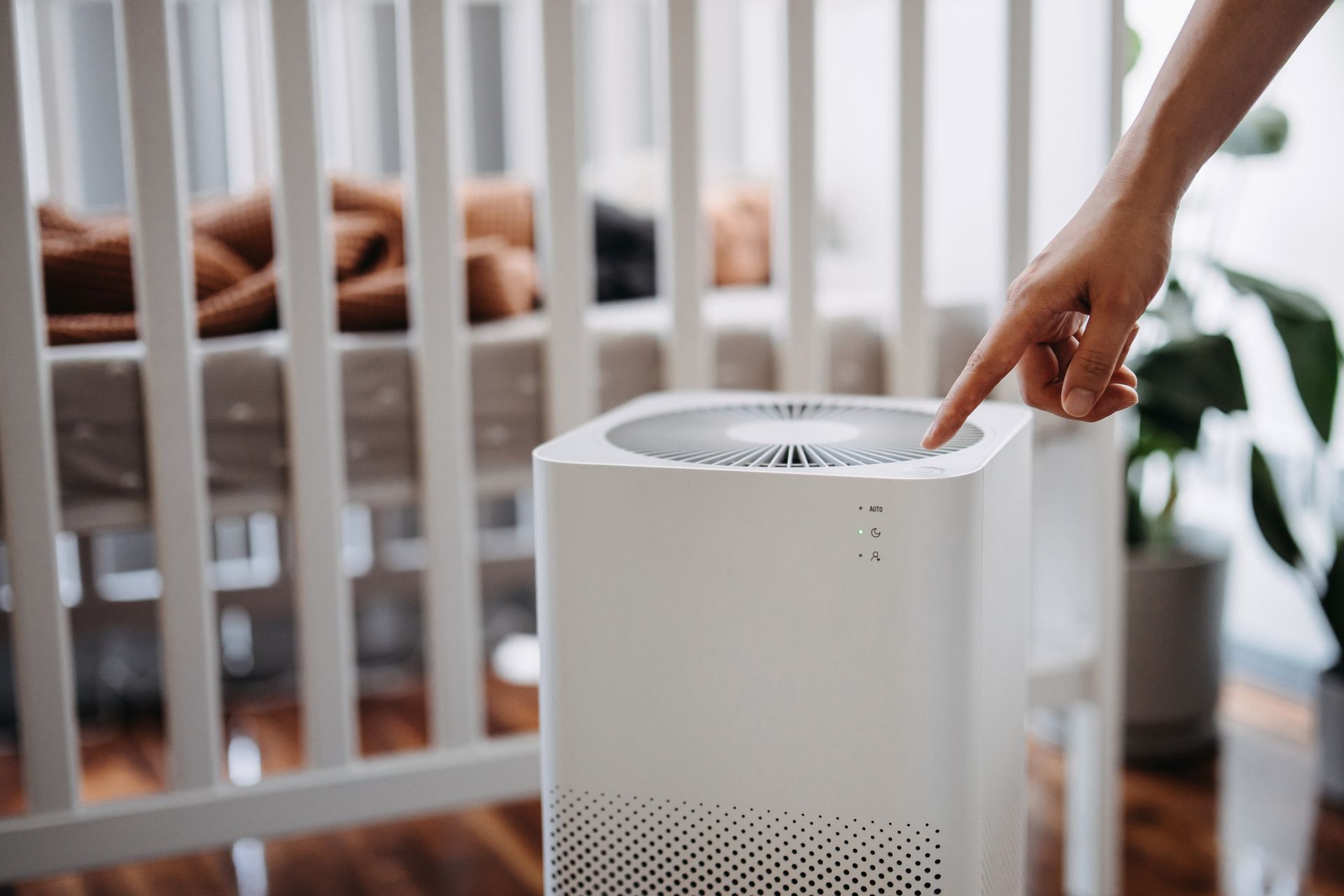 A person is pointing at a air purifier in front of a crib.