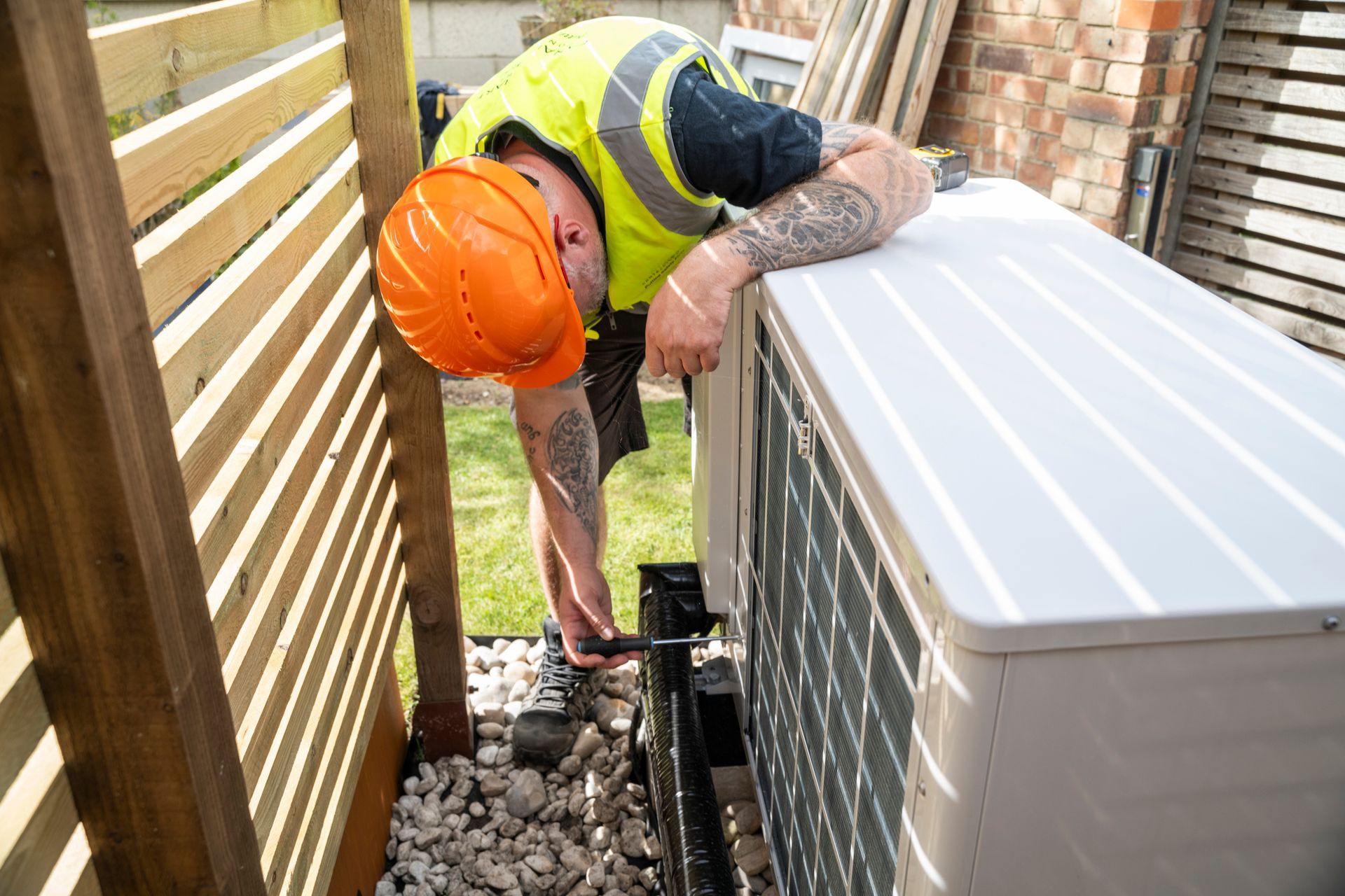 A man wearing a hard hat is working on an air conditioner.