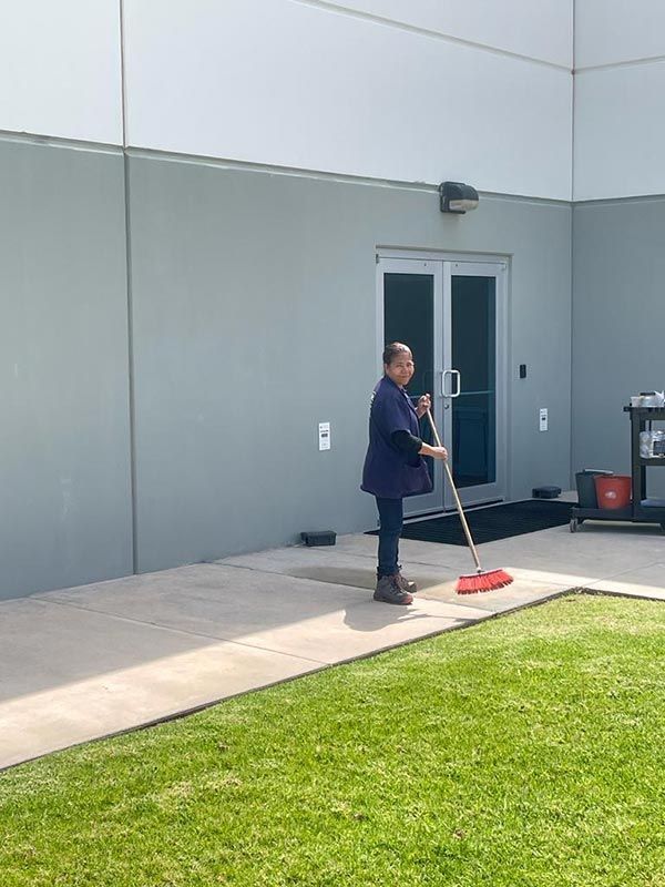 Persona barriendo un patio de concreto afuera de un edificio.