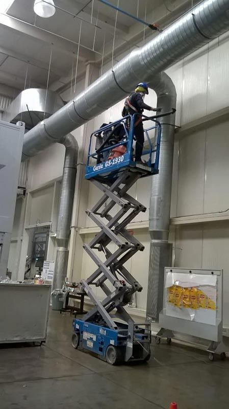 Trabajador en un elevador de tijera, trabajando en conductos en un gran edificio industrial.