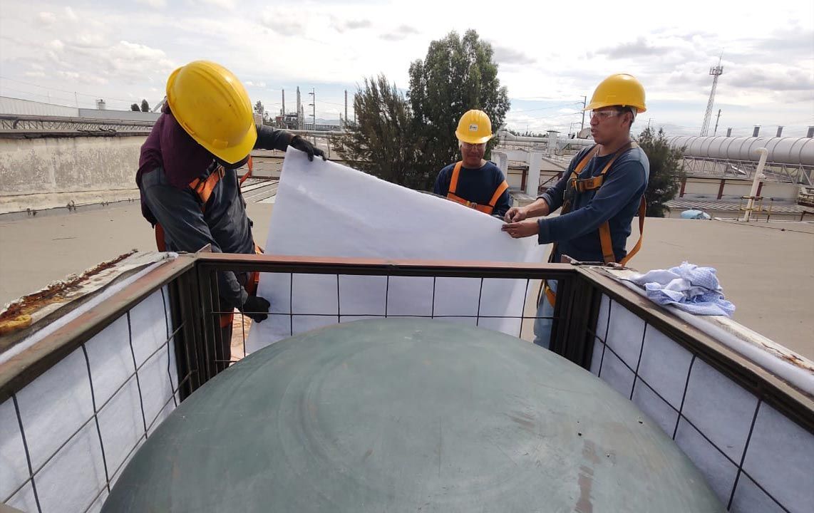 Trabajadores con cascos instalando una sábana blanca sobre una gran estructura en forma de cúpula en un techo.