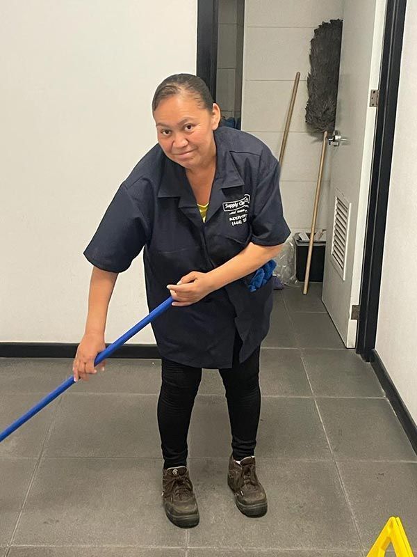 Una mujer con uniforme azul friega el suelo de baldosas de un pasillo.