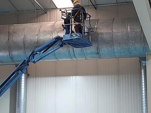 Persona en un ascensor trabajando en grandes conductos metálicos dentro de un edificio.