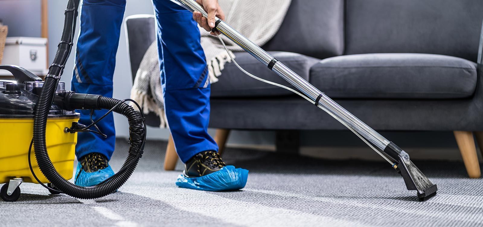 Persona aspirando una alfombra en una sala de estar; utiliza una aspiradora profesional.