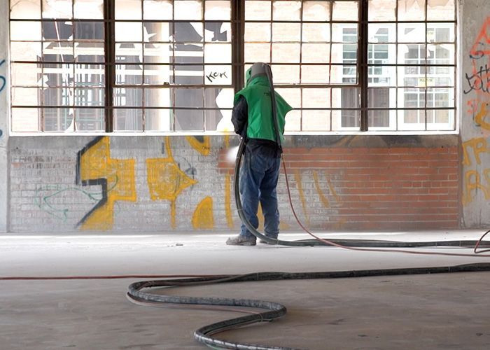 A man is sandblasting a brick wall with graffiti on it.