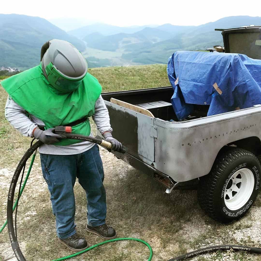 A man in a green vest is sandblasting a truck.