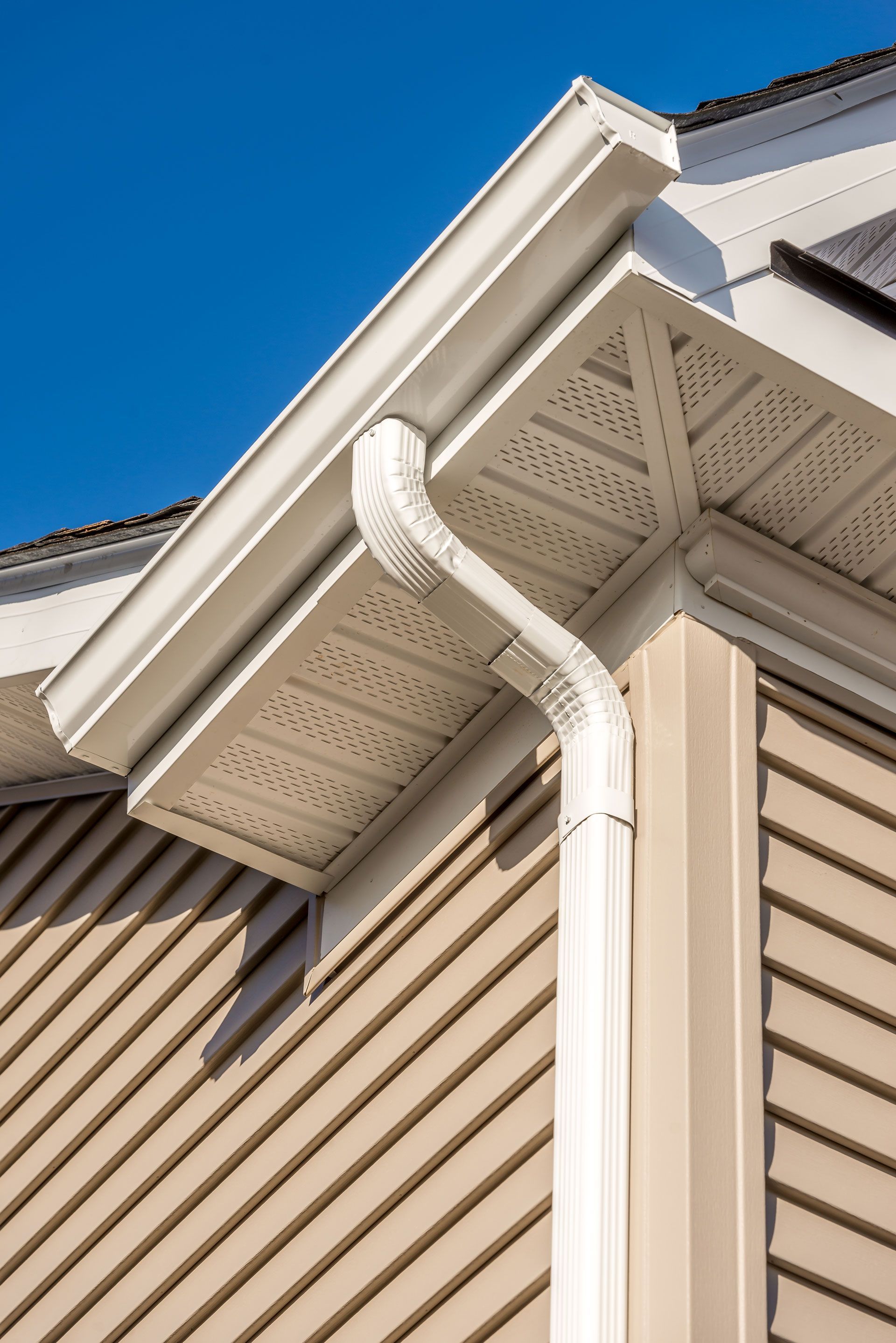 White gutters and downspout on a beige house with blue sky.