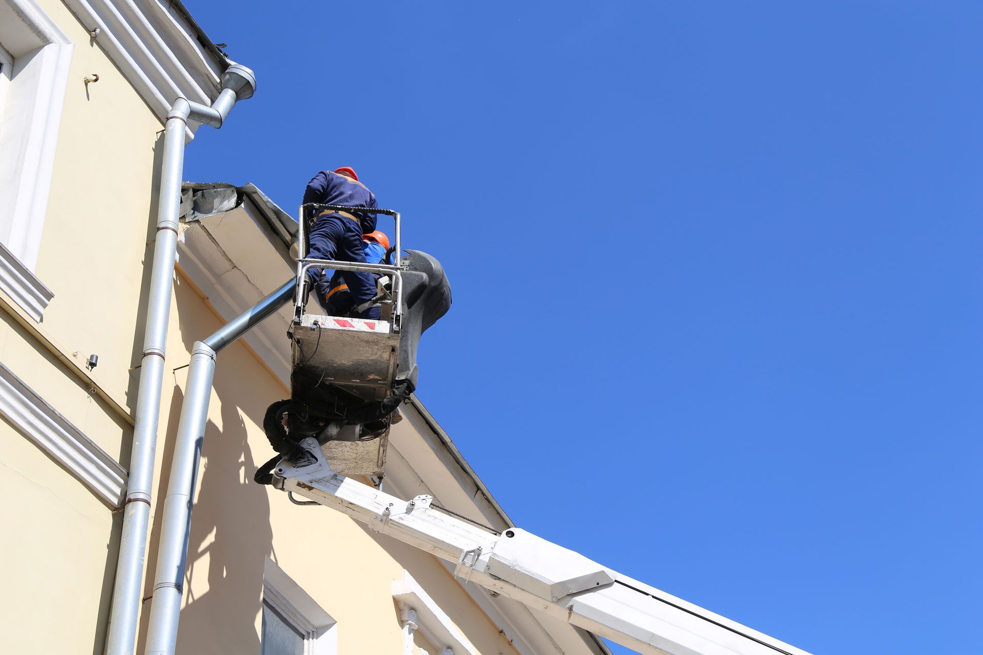 Workers in a lift working on a building's roof under a blue sky.