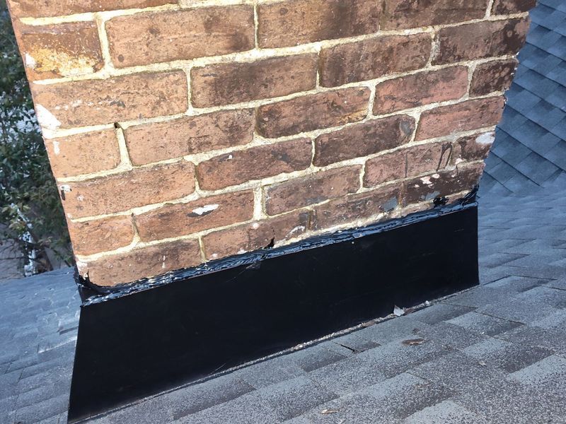 Brick chimney with black flashing on a gray shingle roof
