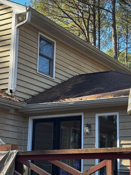 Beige house exterior with a black roof, gutters, window, and door