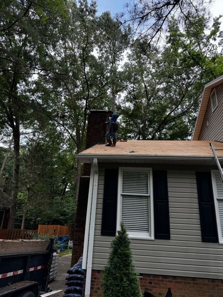 Man on a roof near a chimney working with trees in the background