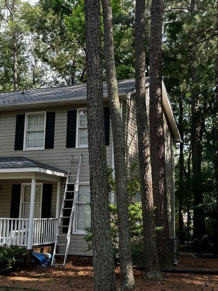 A tall ladder leans against a two-story house with beige siding and black shutters