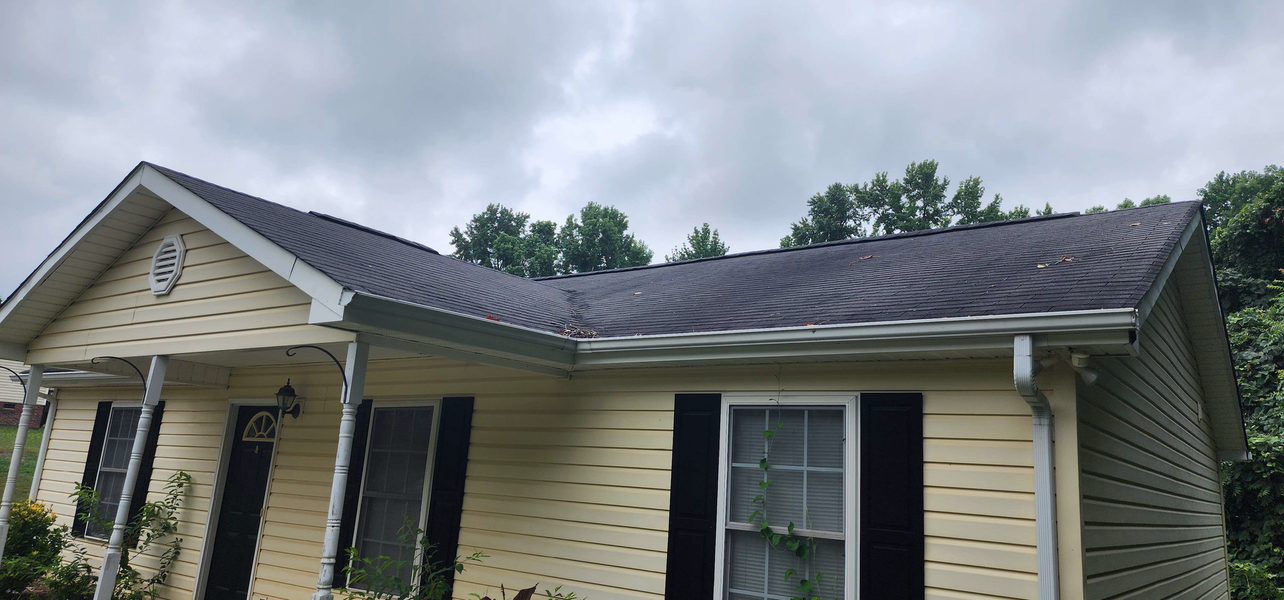 A yellow house with a dark roof and black shutters under a cloudy sky