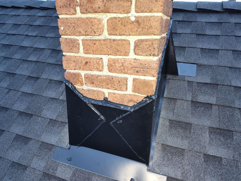 Brick chimney with dark metal flashing on a shingled roof
