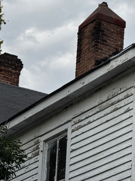 Brick chimneys on a white clapboard building with peeling paint