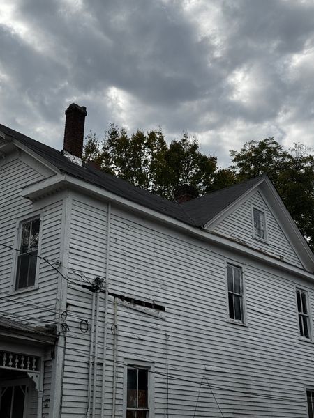 White two-story house with a dark roof and chimney under a cloudy sky
