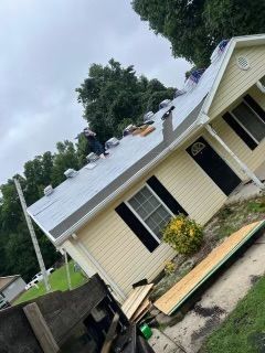 Roofers working on a silver metal roof on a yellow house with black shutters
