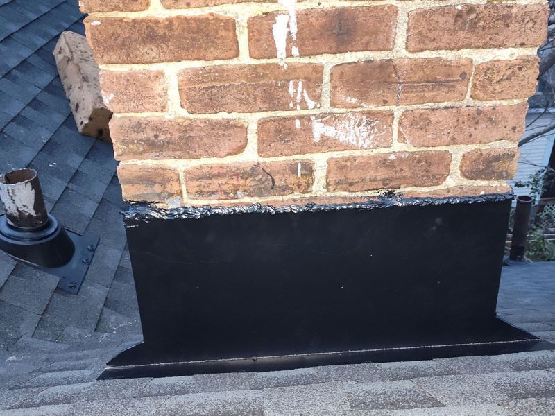 Brick chimney with black flashing on a dark shingled roof