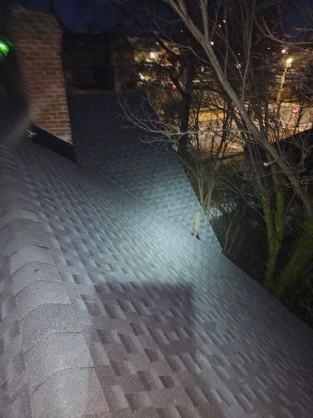 View of dark grey shingled roof with a spotlight and a brick chimney