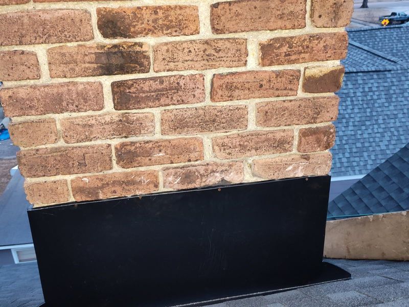 Brick chimney with black flashing on a gray shingle roof