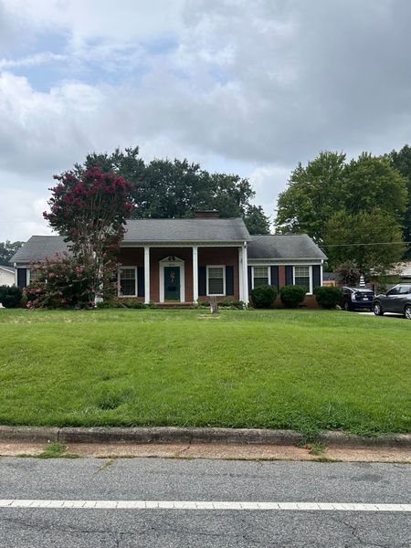 A single-story brick house with a large green lawn and white columns