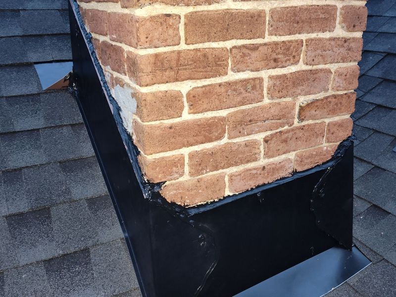 Brick chimney with black flashing on a gray shingle roof