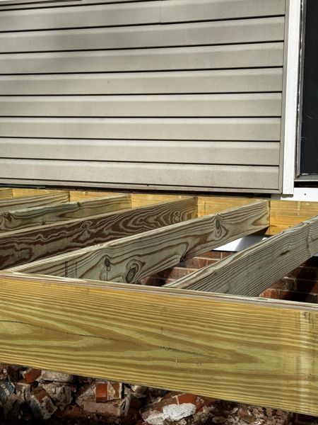 Wooden deck frame against a brick foundation and beige siding