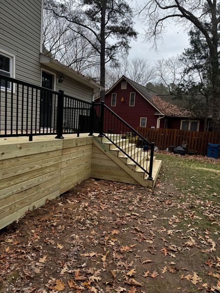 New wooden deck with black railings and stairs, next to a house and a red building