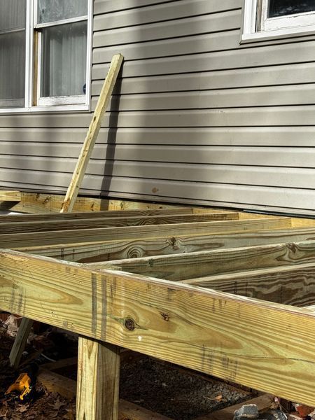 Wooden deck under construction near a house with gray siding and windows