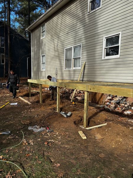 Men constructing a wooden deck attached to a two-story house in an outdoor setting