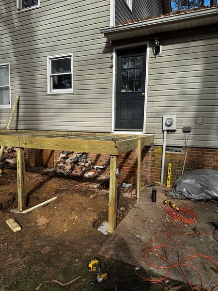 A partially-built wooden deck next to a house with a black door