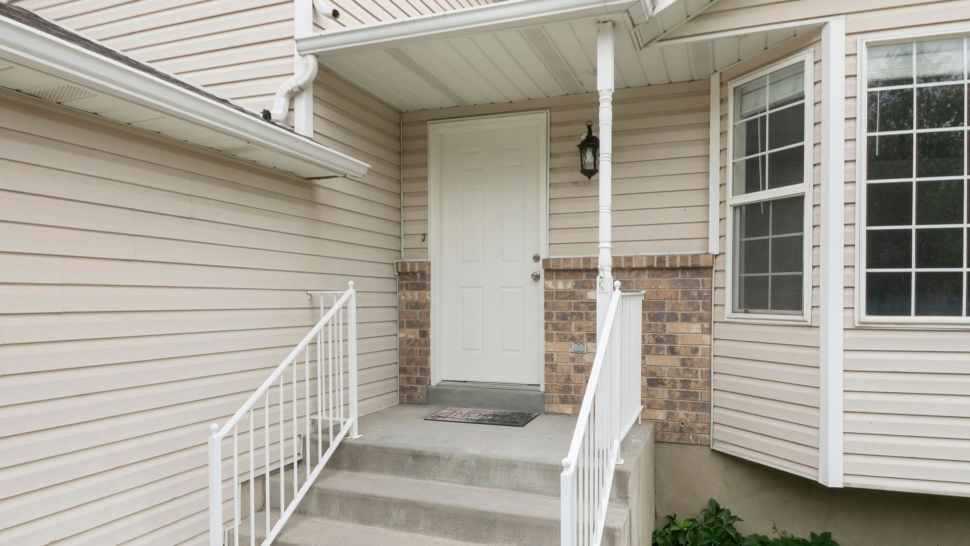 Front entrance of a house with white door, steps, and railings. Beige siding and a small porch.
