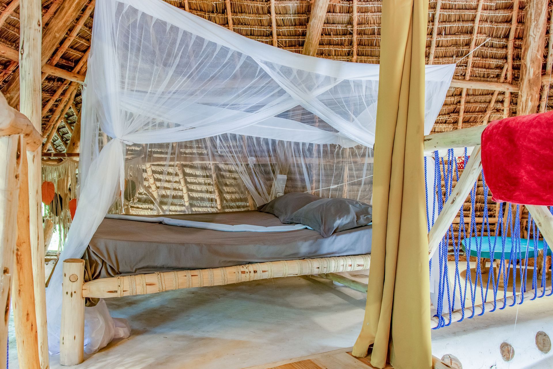 Bed in a rustic room with a mosquito net, wooden beams, and a thatched roof.