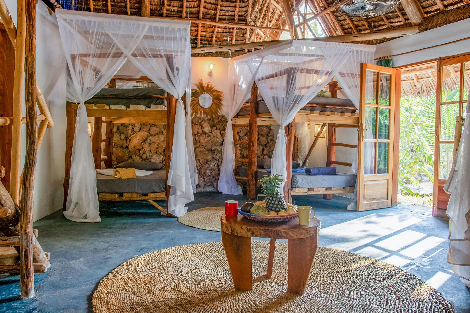 Rustic bedroom with two bunk beds draped with mosquito nets; pineapple on a wooden table.