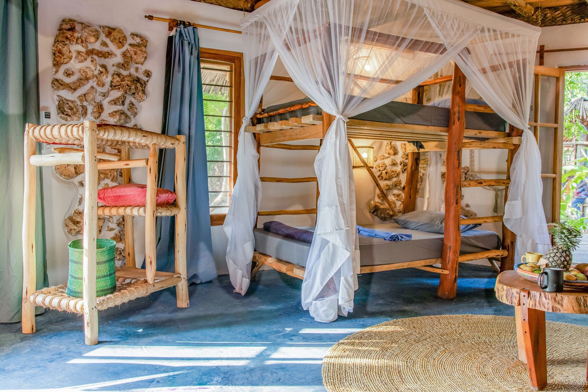 Cozy room with bunk bed, mosquito net, wooden furniture, and a natural stone wall.