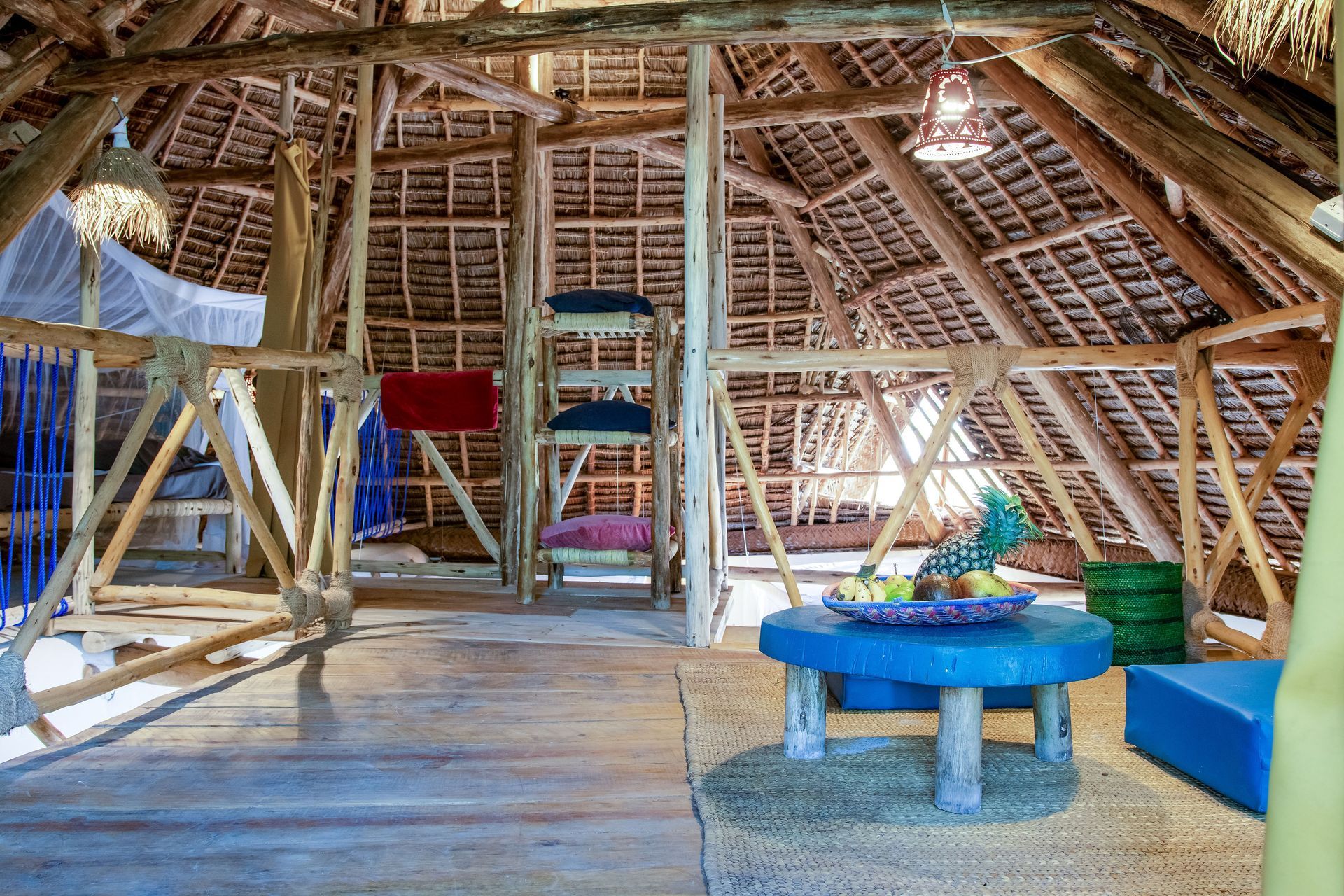 Rustic wooden loft interior with natural thatch roof, blue furniture, and fruit.