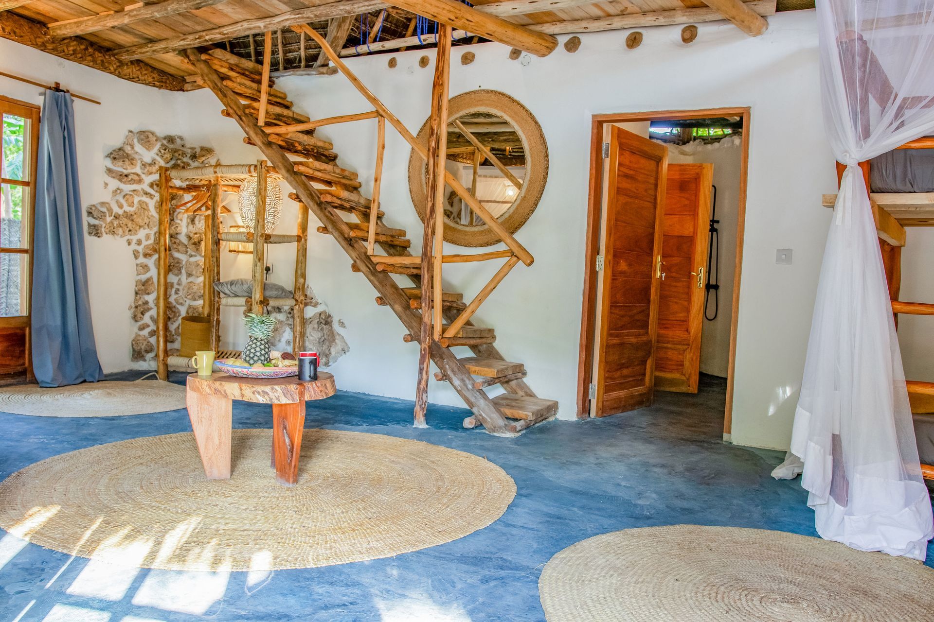 Rustic living room with wooden stairs, a large round mirror, and woven rugs.
