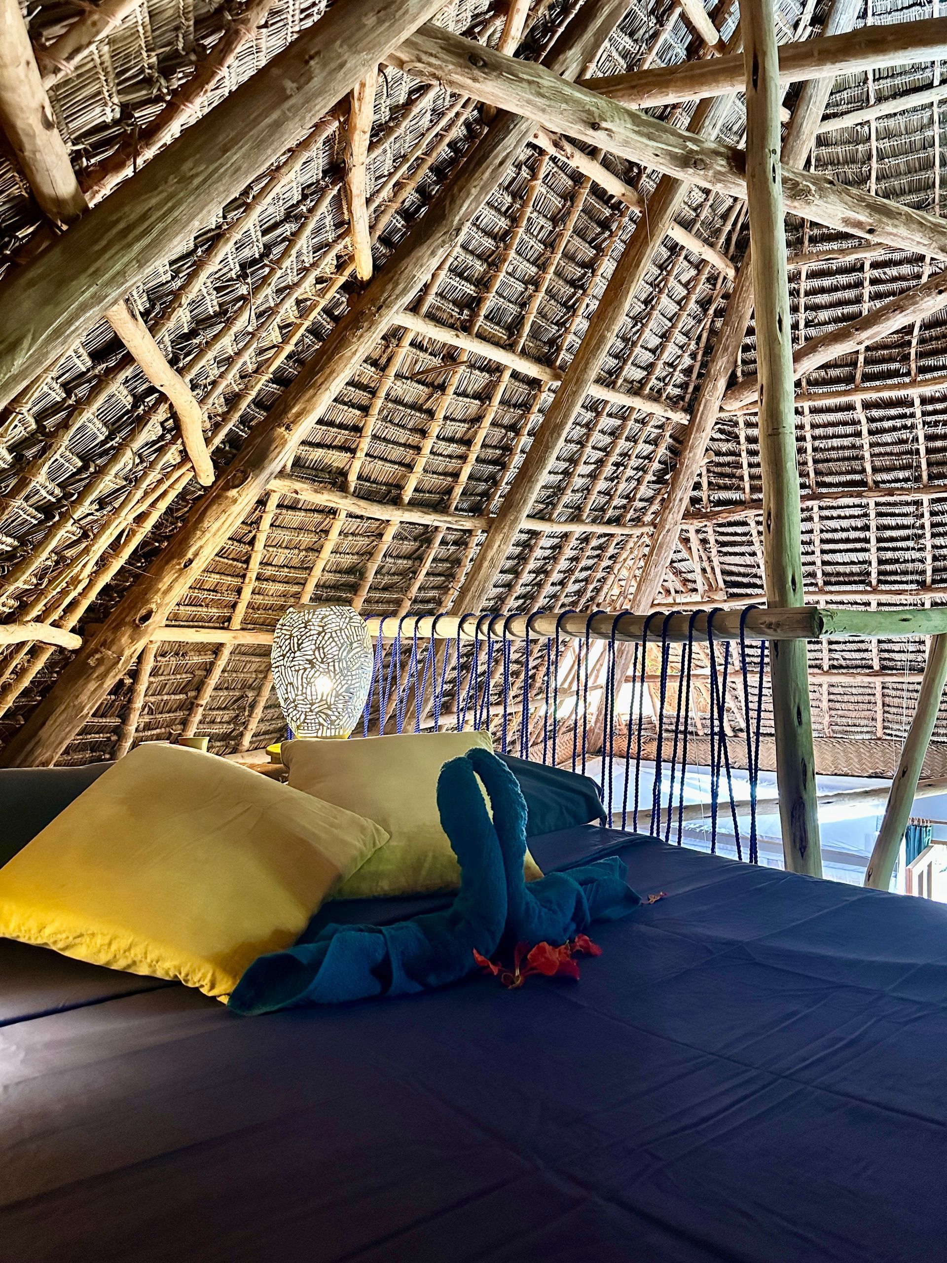 Bed with pillows under thatched roof.