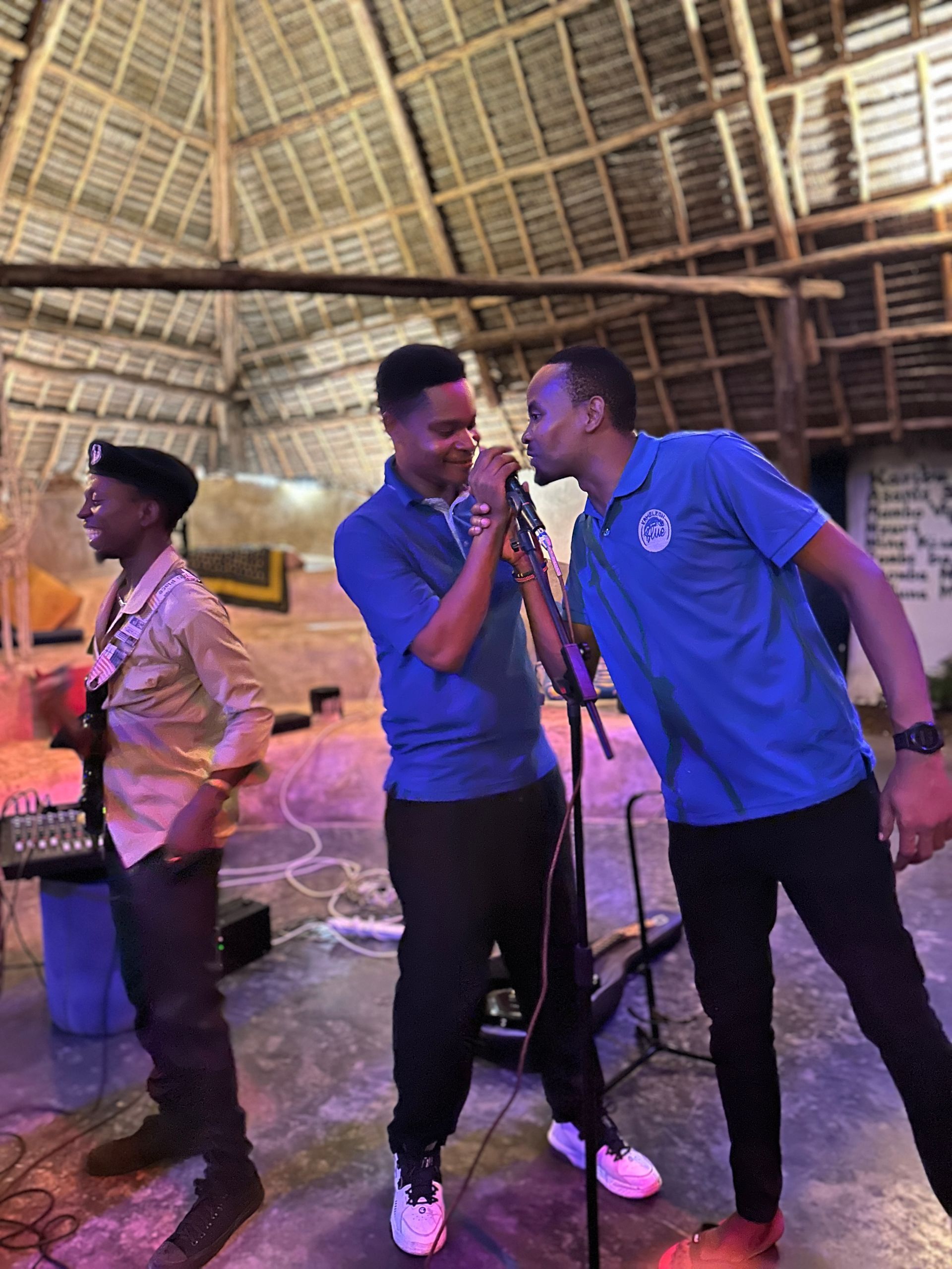 Three men are singing into microphones in a room.