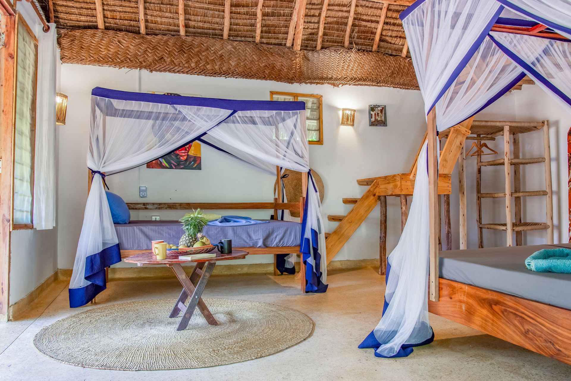 Bedroom with two beds, mosquito nets, wooden decor, and a small table with food.