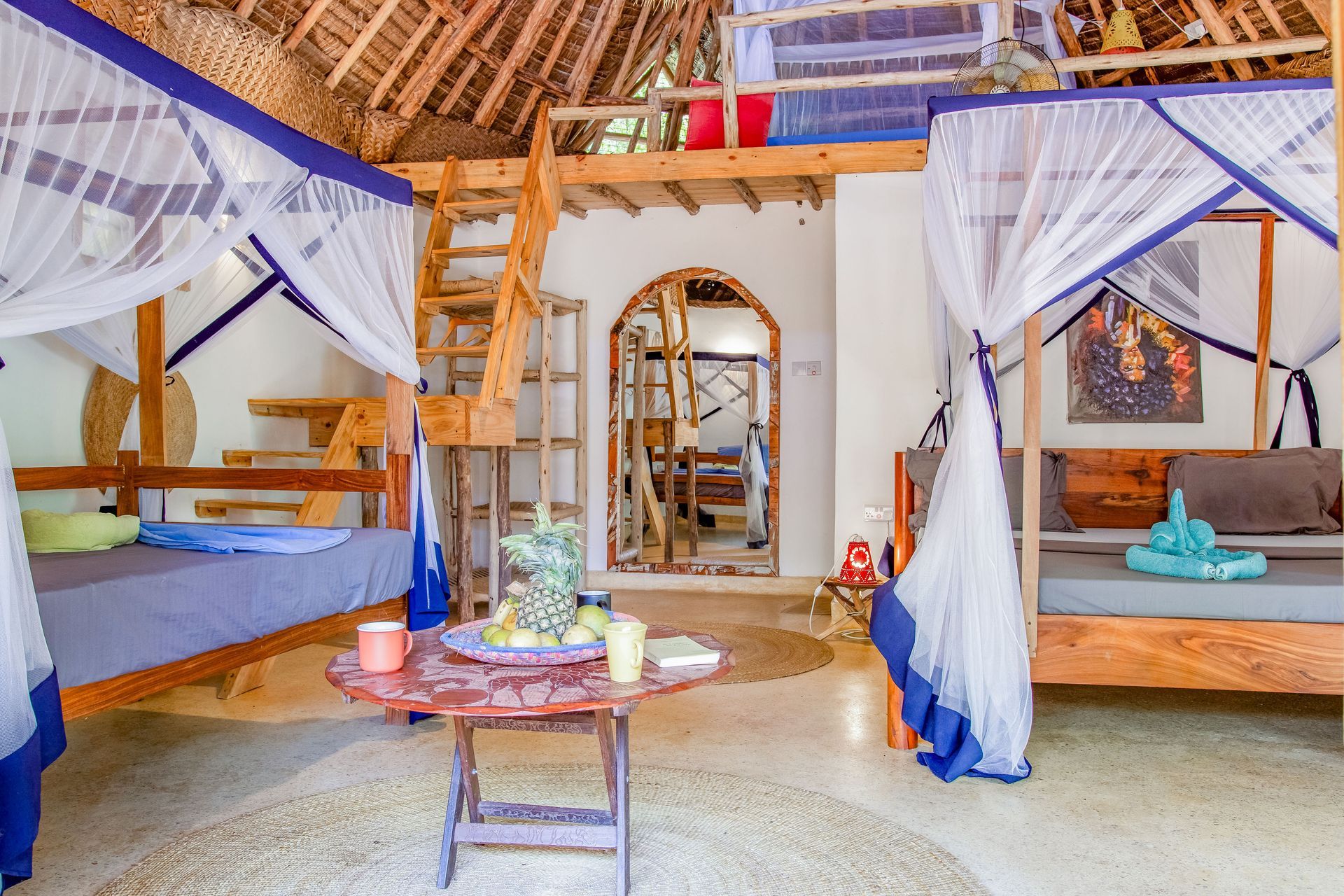 Cozy interior with multiple beds, mosquito nets, wooden furniture, and a loft. Bright, airy, and tropical.