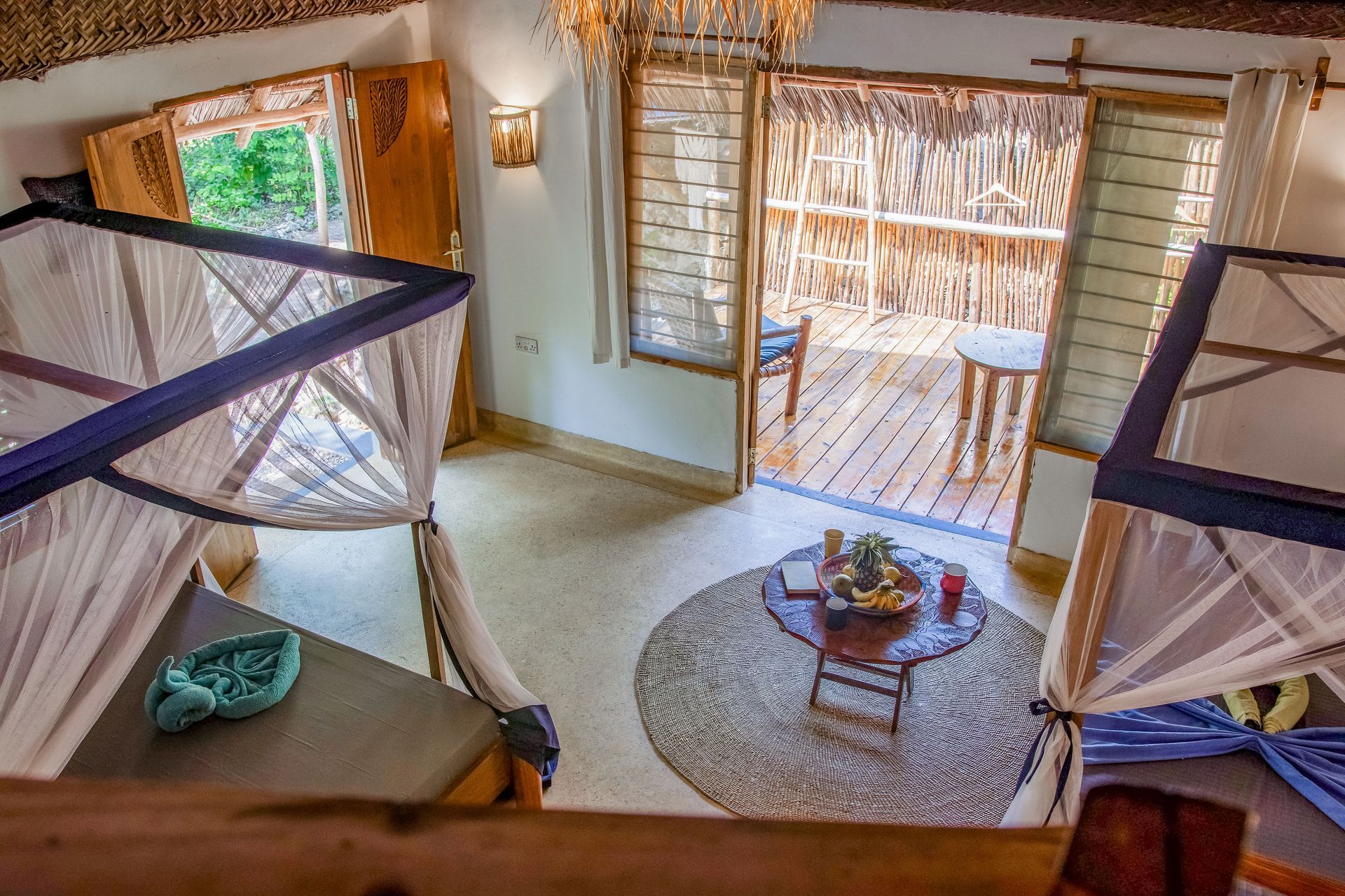 Bedroom with two beds, mosquito nets, thatched roof, and balcony access.